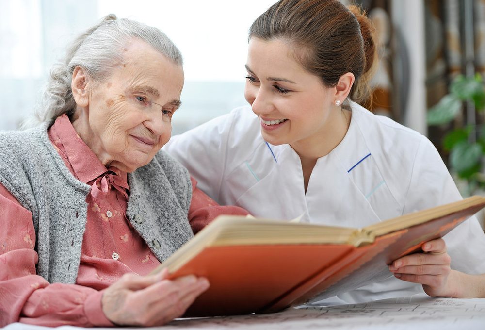 A volunteer sitting with an older neighbour, reading together.