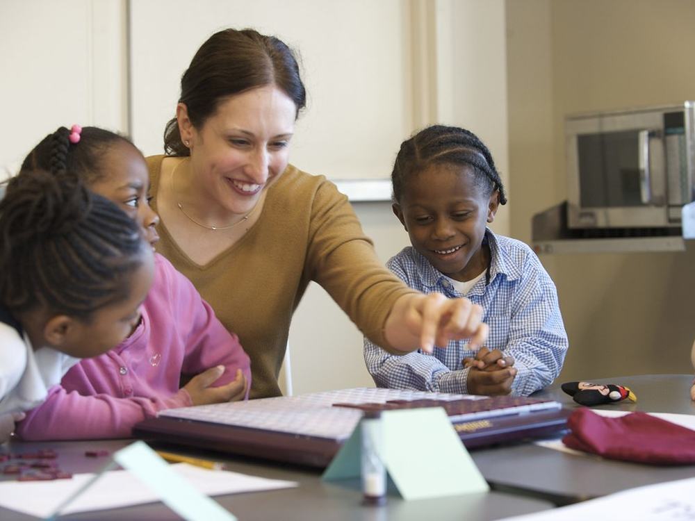 An adult and two children work through a lesson together at one table.